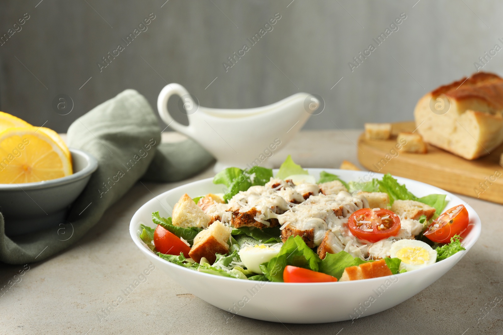 Photo of Tasty Caesar salad with chicken and tomatoes in bowl on gray textured table