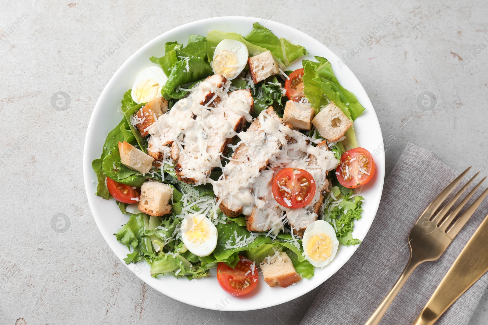 Photo of Tasty Caesar salad with chicken and tomatoes in bowl served on gray textured table, flat lay