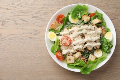 Photo of Tasty Caesar salad with chicken and tomatoes in bowl on wooden table, top view. Space for text