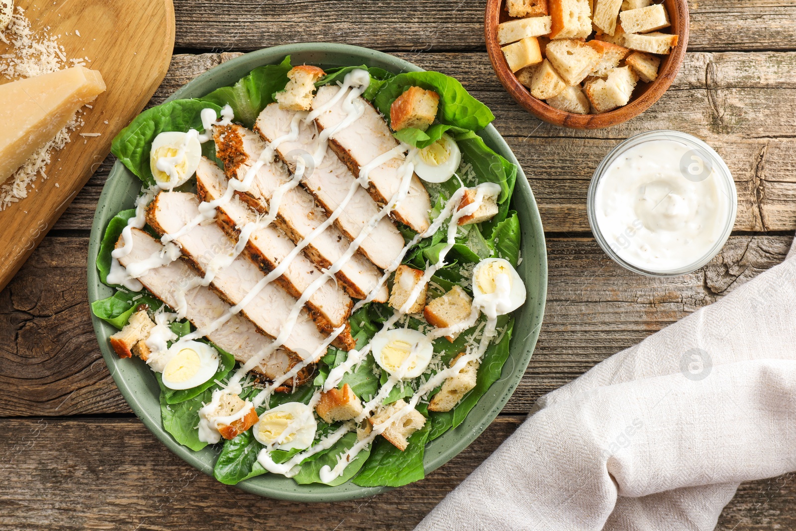 Photo of Delicious Caesar salad with chicken and other ingredients on wooden table, flat lay