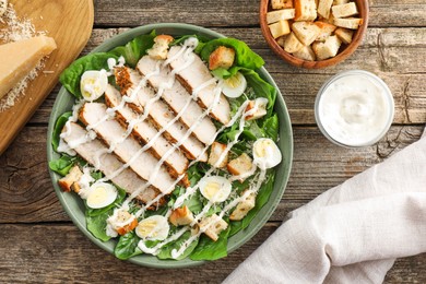 Photo of Delicious Caesar salad with chicken and other ingredients on wooden table, flat lay