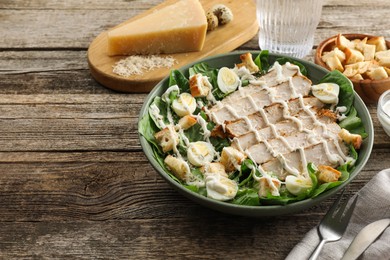 Photo of Delicious Caesar salad with chicken on wooden table, closeup. Space for text