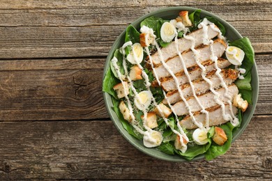 Photo of Delicious Caesar salad with chicken on wooden table, top view. Space for text