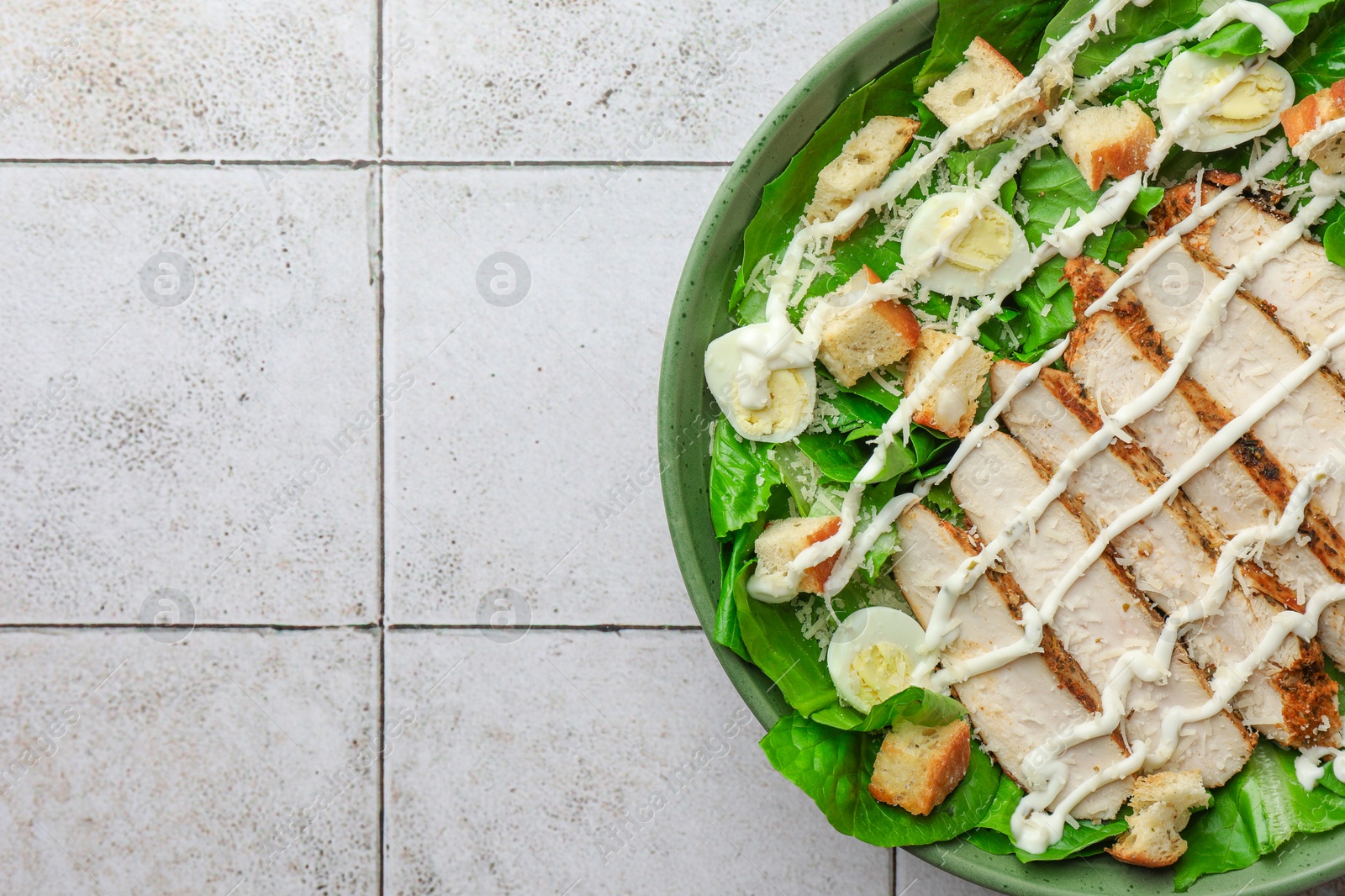 Photo of Delicious Caesar salad with chicken on textured tiled table, top view. Space for text