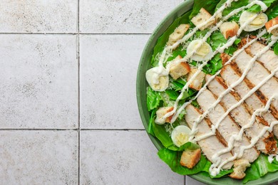 Photo of Delicious Caesar salad with chicken on textured tiled table, top view. Space for text