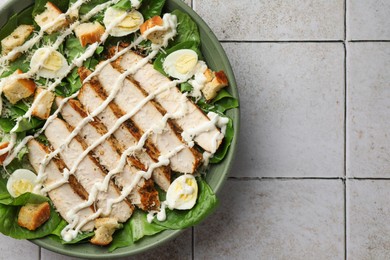 Photo of Delicious Caesar salad with chicken on textured tiled table, top view. Space for text