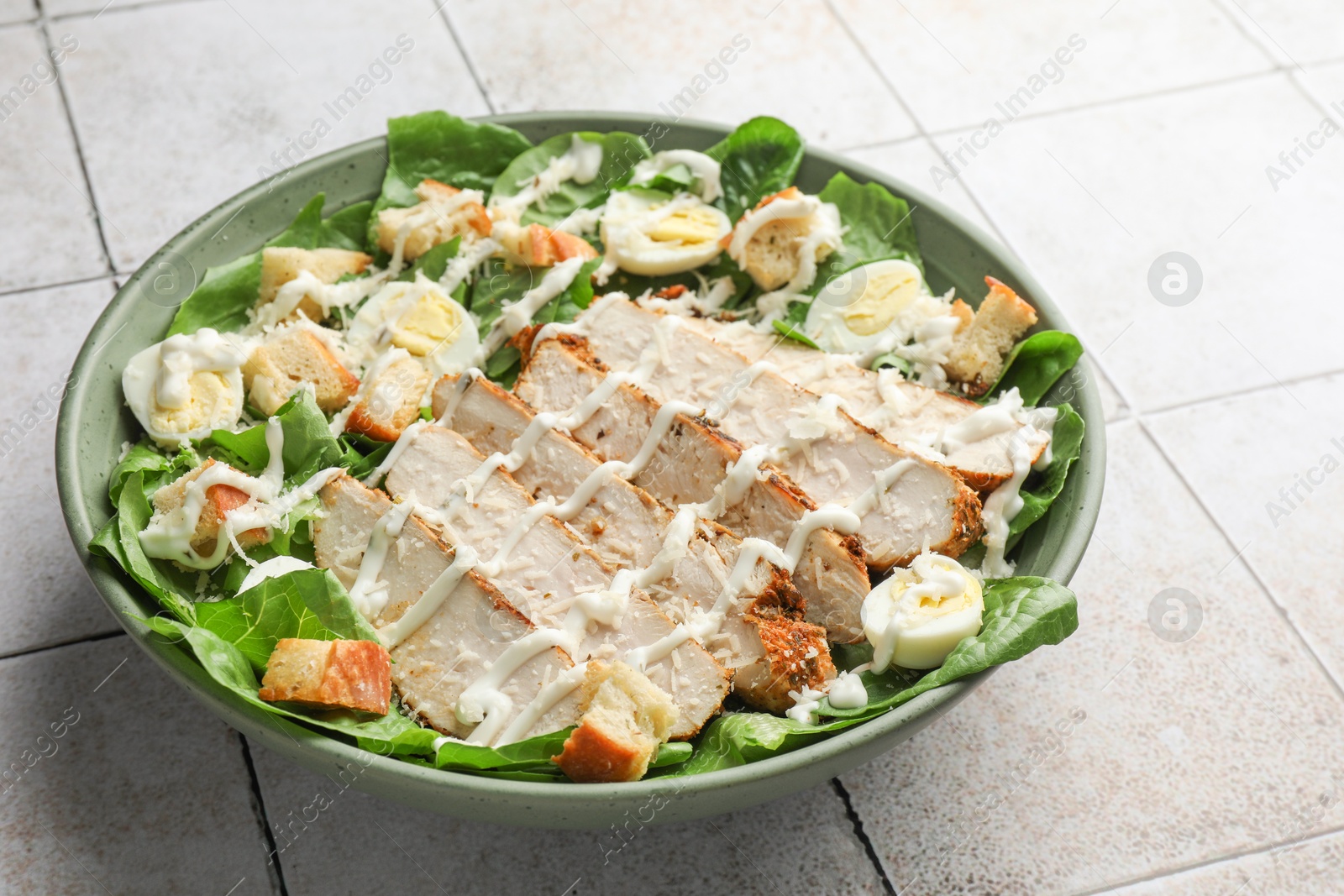 Photo of Delicious Caesar salad with chicken on textured tiled table, closeup