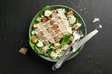 Photo of Delicious Caesar salad with chicken on black textured table, top view