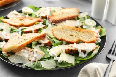 Photo of Delicious Caesar salad with chicken on grey textured table, closeup