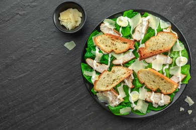 Photo of Delicious Caesar salad with chicken and cheese on black textured table, flat lay. Space for text