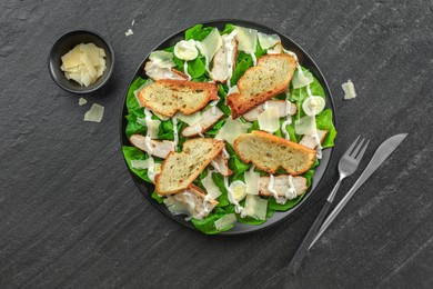 Photo of Delicious Caesar salad with chicken and cheese on black textured table, flat lay