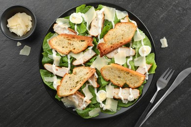 Photo of Delicious Caesar salad with chicken and cheese on black textured table, flat lay