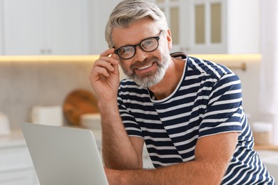 Photo of Happy middle aged man using laptop in kitchen