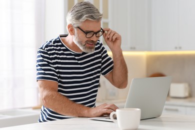 Photo of Happy middle aged man using laptop at white marble table in kitchen