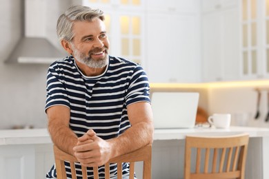 Photo of Happy middle aged man on chair in kitchen, space for text