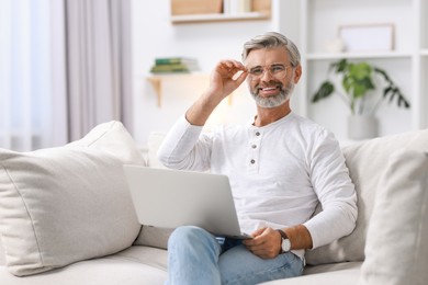 Photo of Happy middle aged man with laptop on sofa at home