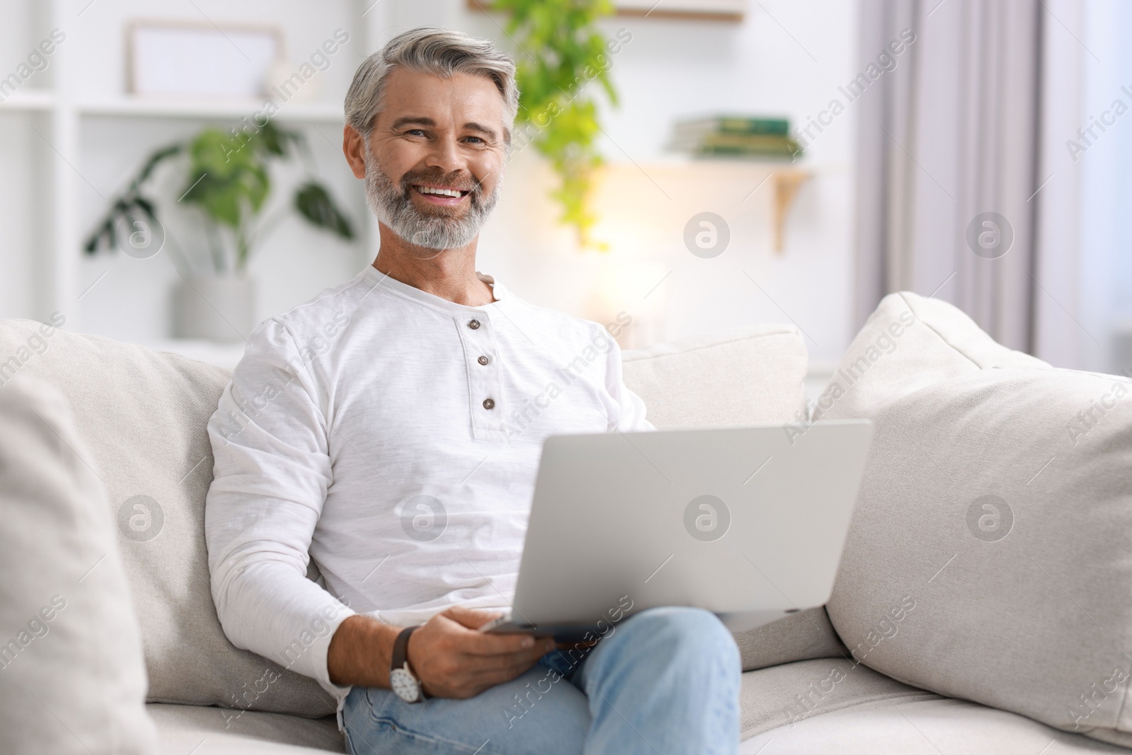 Photo of Happy middle aged man with laptop on sofa at home