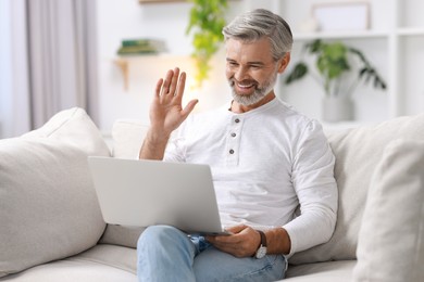 Photo of Happy middle aged man having video chat via laptop on sofa indoors