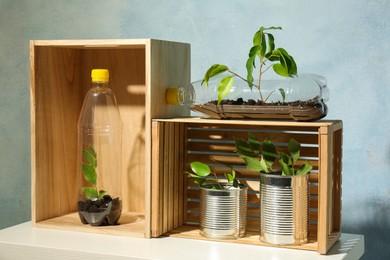 Photo of Recycling concept. Metal cans and plastic bottles with growing plants on white table