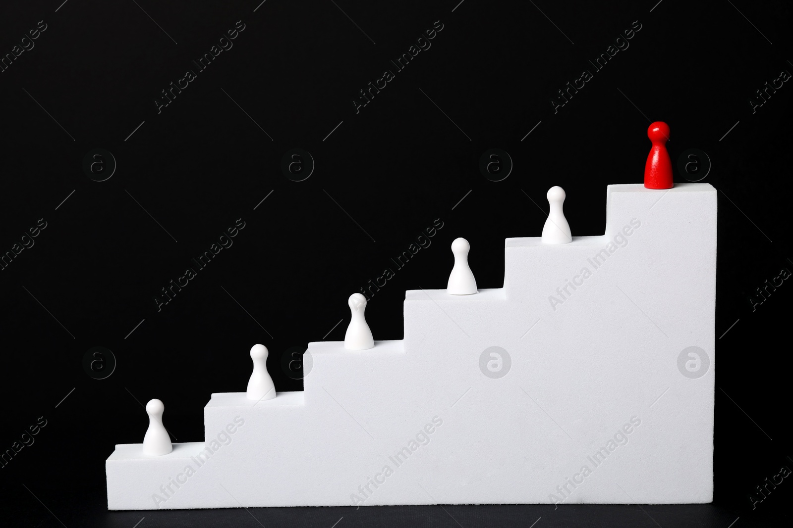 Photo of Winner. Red piece among white ones on stairs against black background