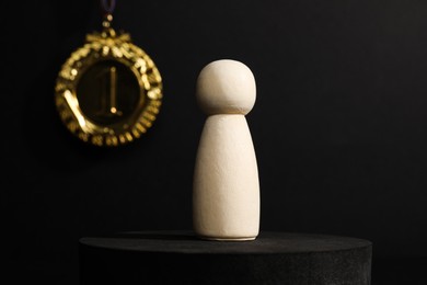 Photo of Winner concept. Wooden figure on podium and golden medal against black background, selective focus