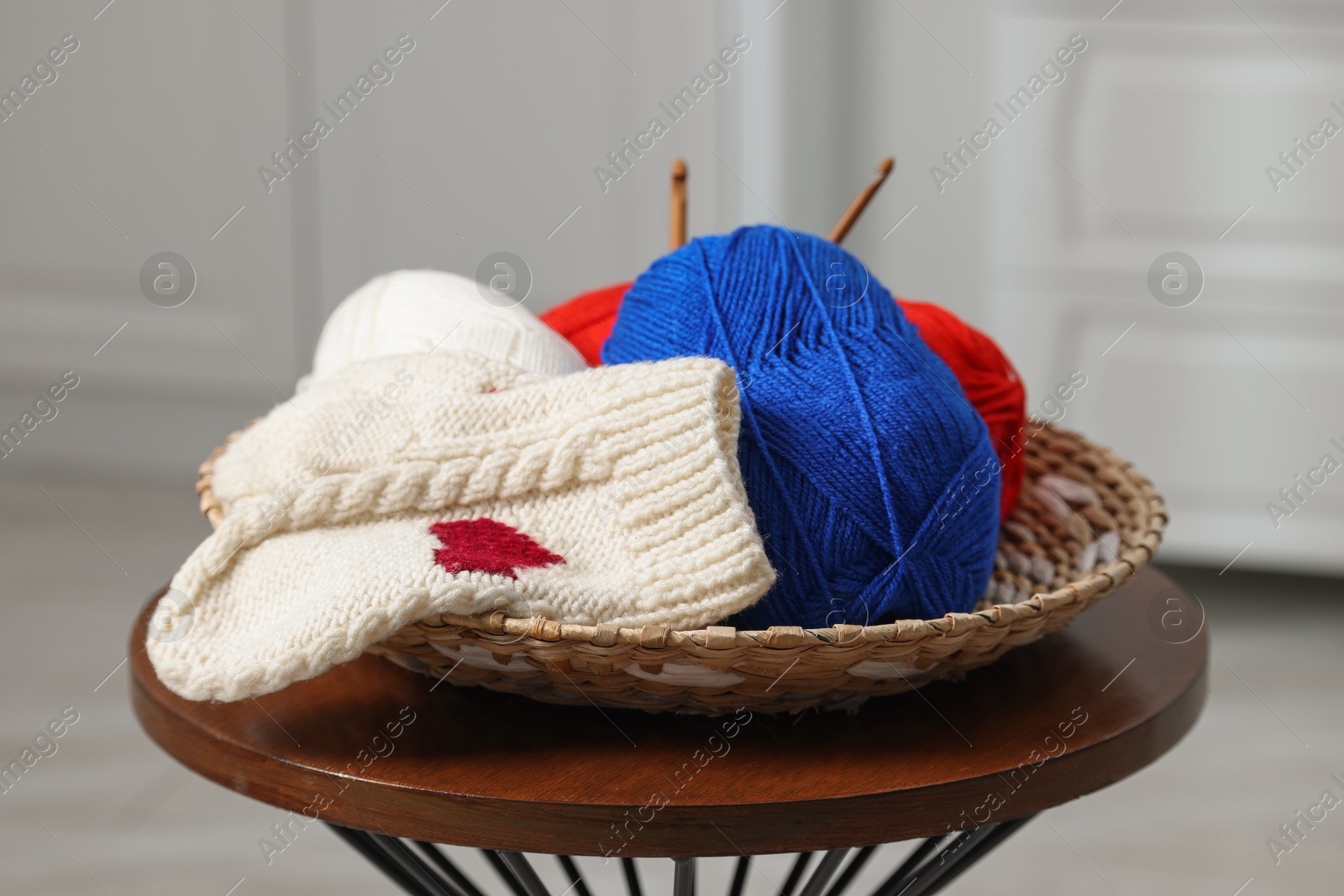 Photo of Skeins of soft yarn, crochet hooks and mittens on coffee table indoors