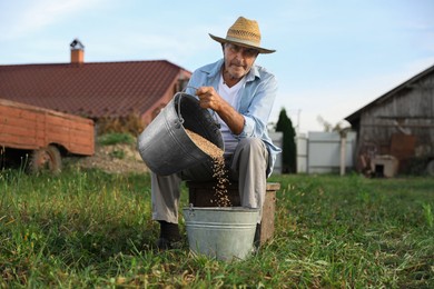 Photo of Senior man pouring wheat grains into bucket outdoors