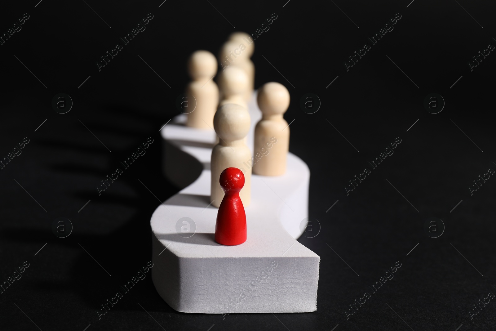 Photo of Winner concept. Red piece among wooden ones on podium against black background, selective focus