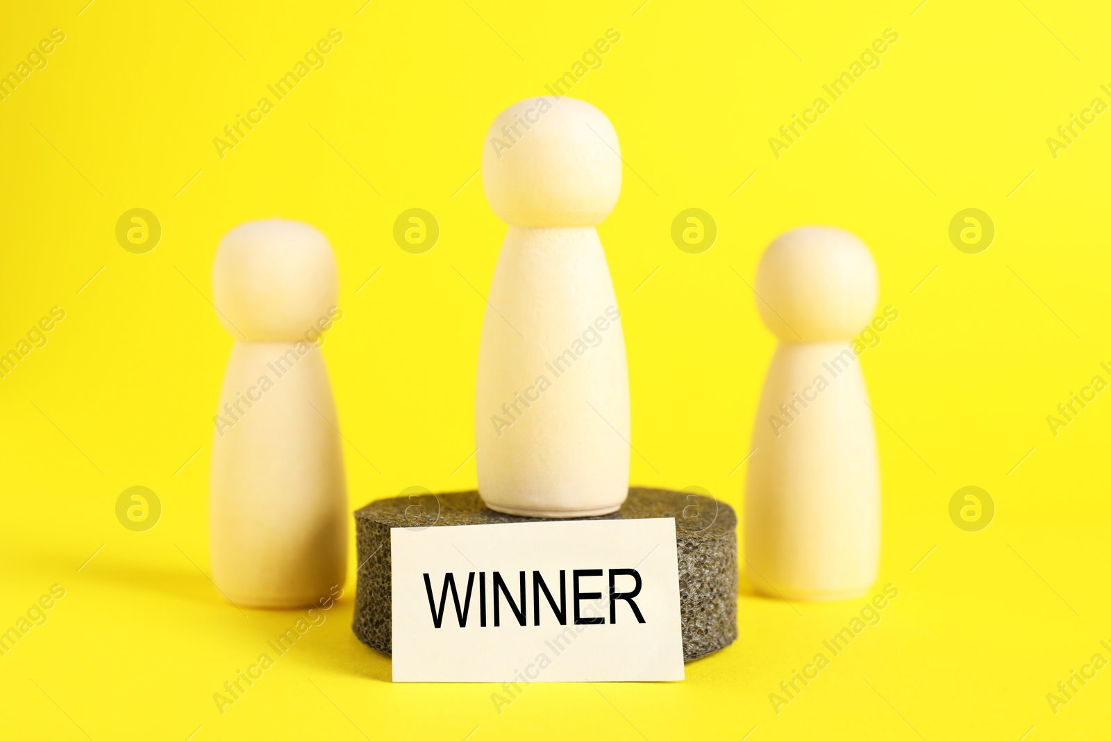 Photo of Winner. One wooden figure on podium among others against yellow background