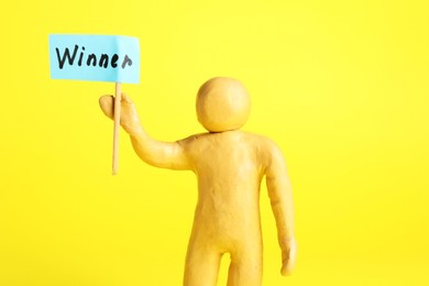 Photo of Human figure holding wooden stick with word Winner on yellow background