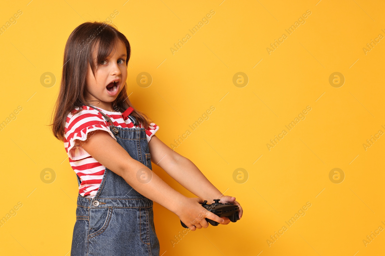 Photo of Emotional little girl with controller on orange background. Space for text