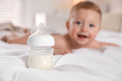 Photo of Cute little baby on bed indoors, focus on bottle of milk