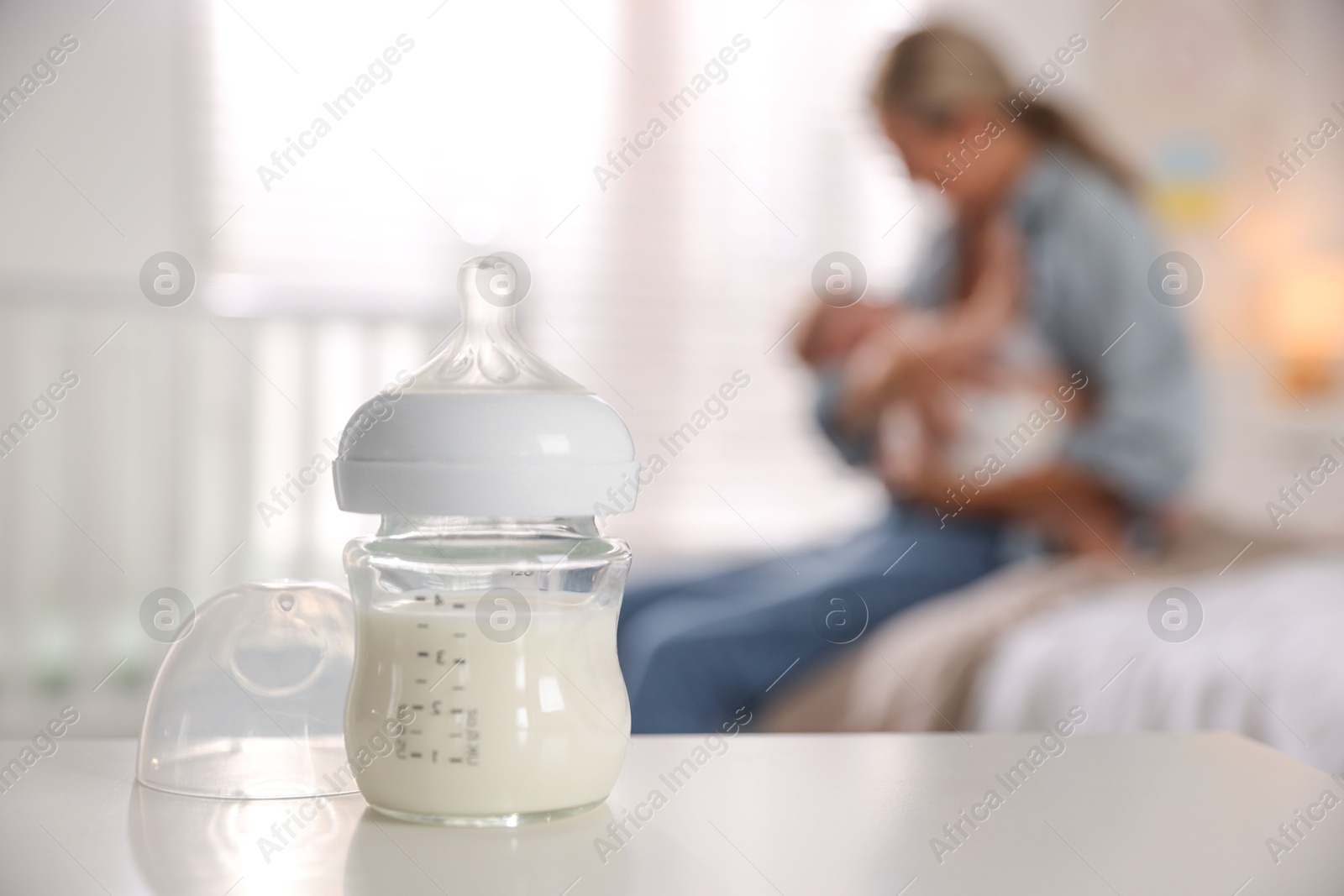 Photo of Mother holding her cute little baby indoors, focus on bottle with milk