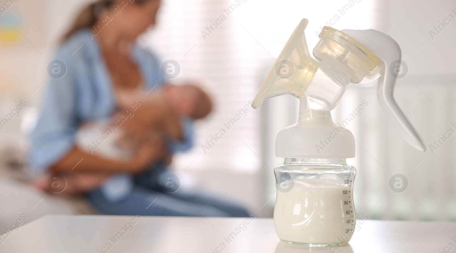 Photo of Mother holding her cute little baby indoors, focus on breast pump with milk