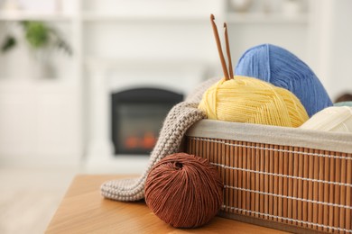 Photo of Colorful yarns, knitting sample, crochet hooks and basket on wooden table indoors, closeup. Space for text