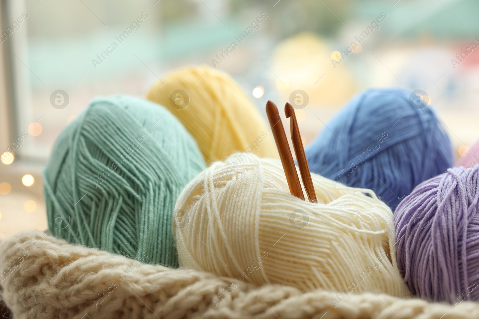 Photo of Many colorful yarns, crochet hooks and sweater on blurred background, closeup