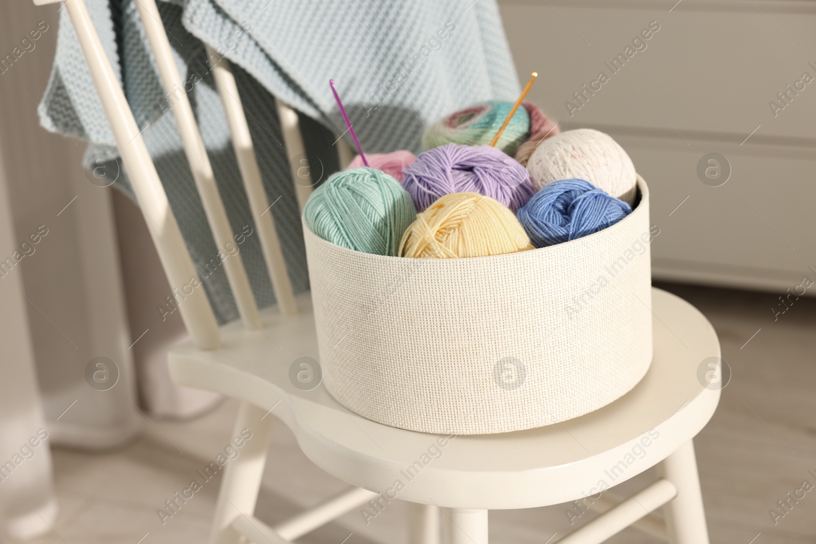 Photo of Box with colorful yarns and crochet hooks on chair indoors