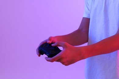 Photo of Teenage boy playing video game with controller on violet background, closeup. Space for text