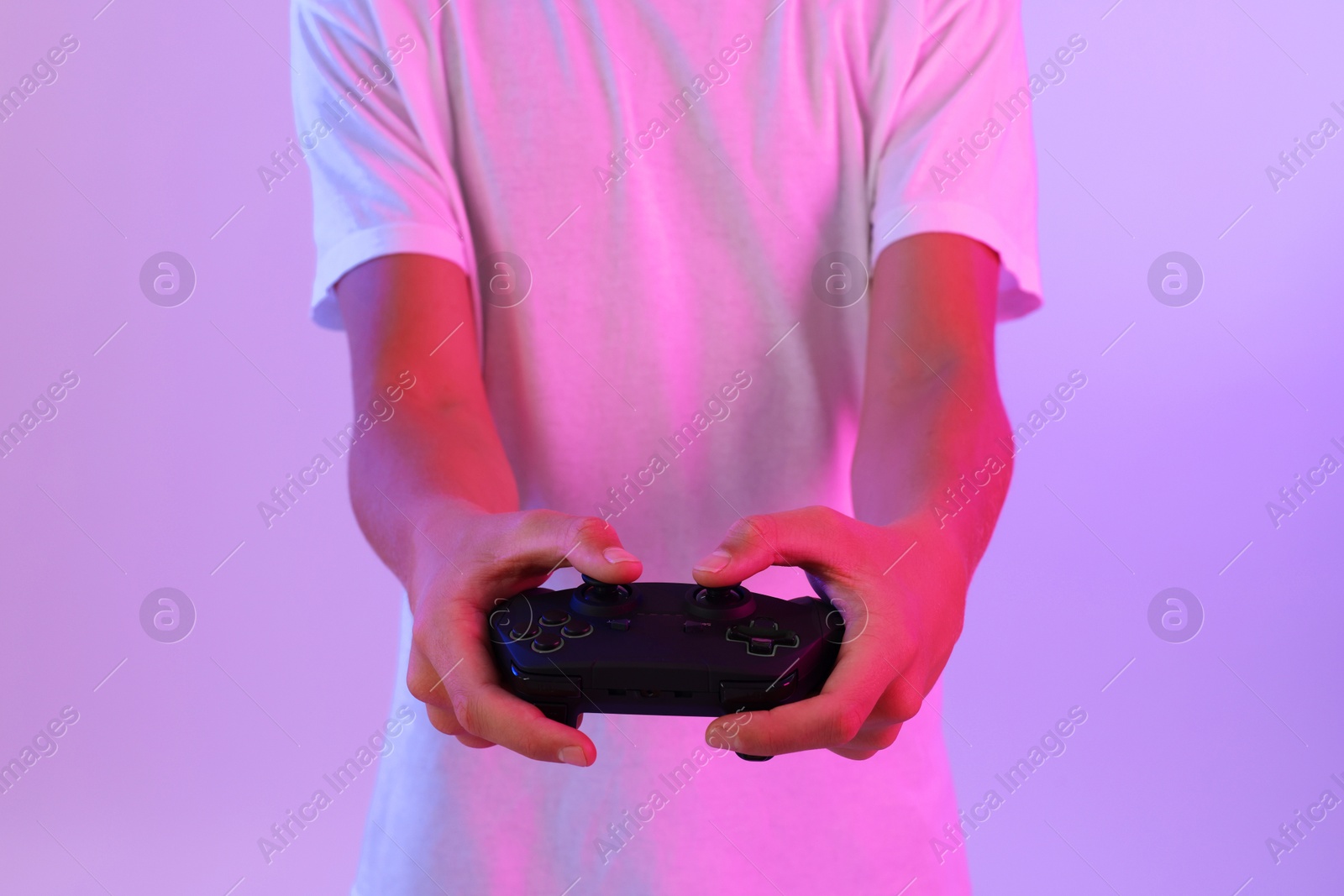 Photo of Teenage boy playing video game with controller on violet background, closeup