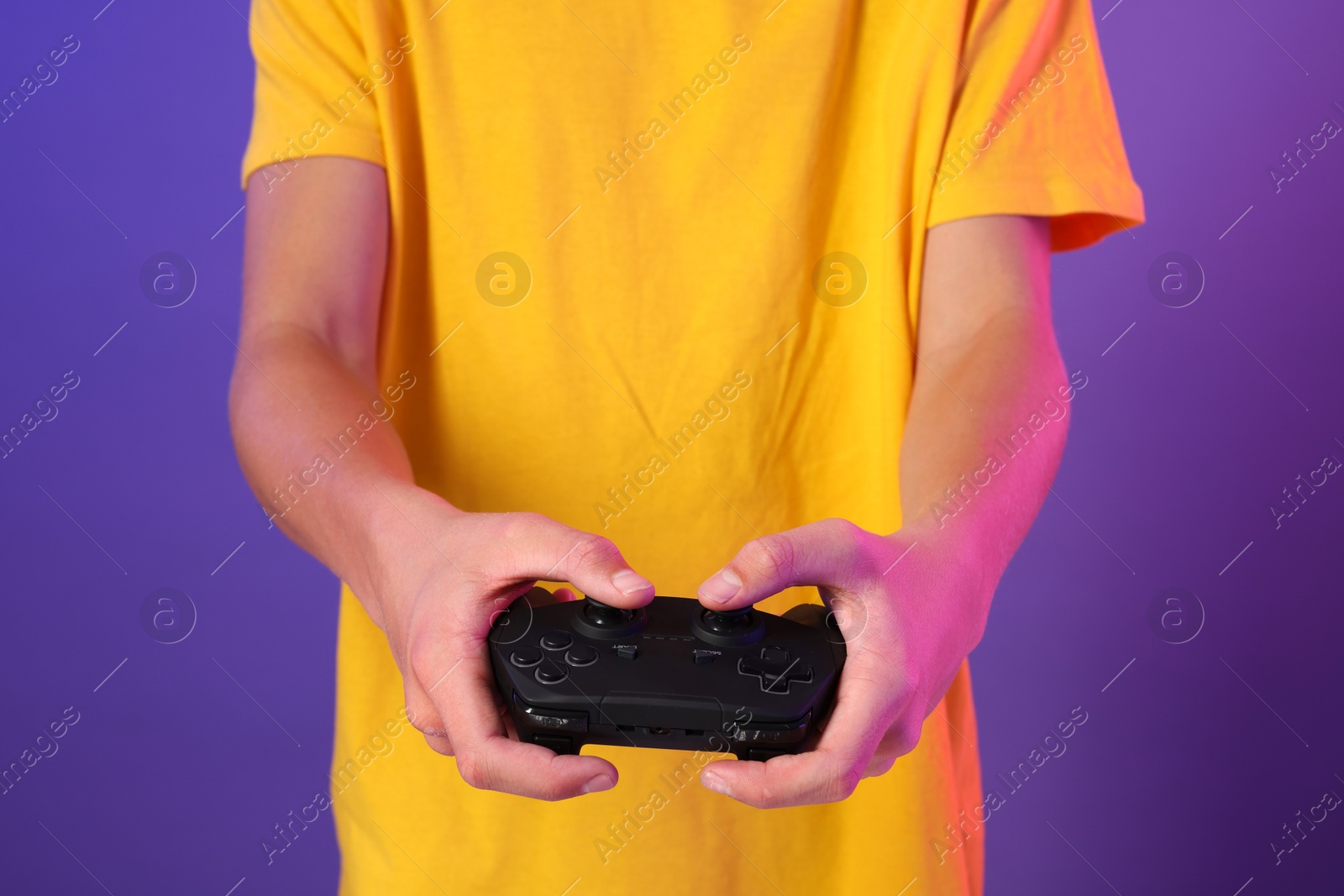 Photo of Teenage boy playing video game with controller on purple background, closeup