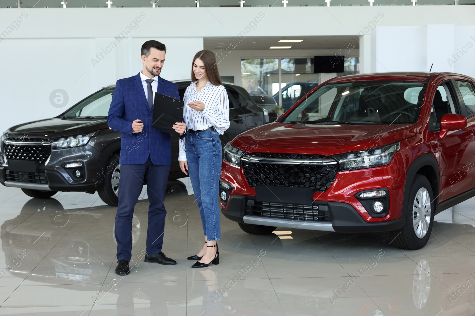 Photo of Salesman and client near new red car in salon