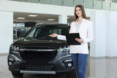 Photo of Happy saleswoman near new black car in salon