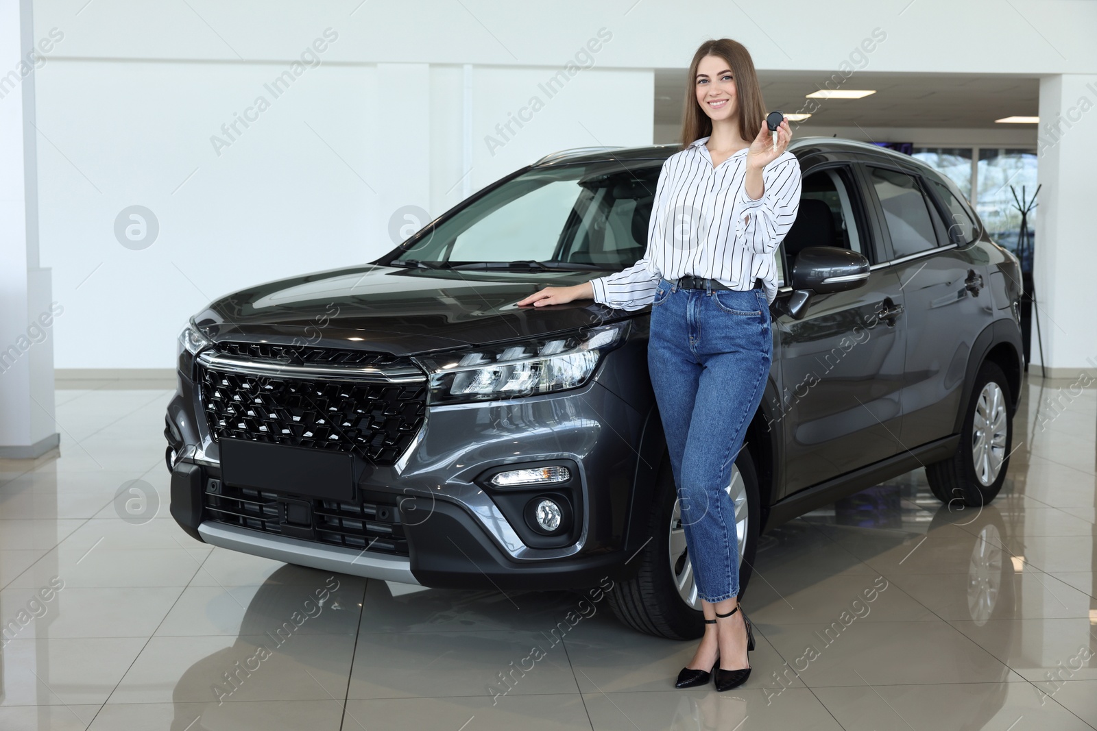 Photo of Happy young woman holding key near new black car in salon