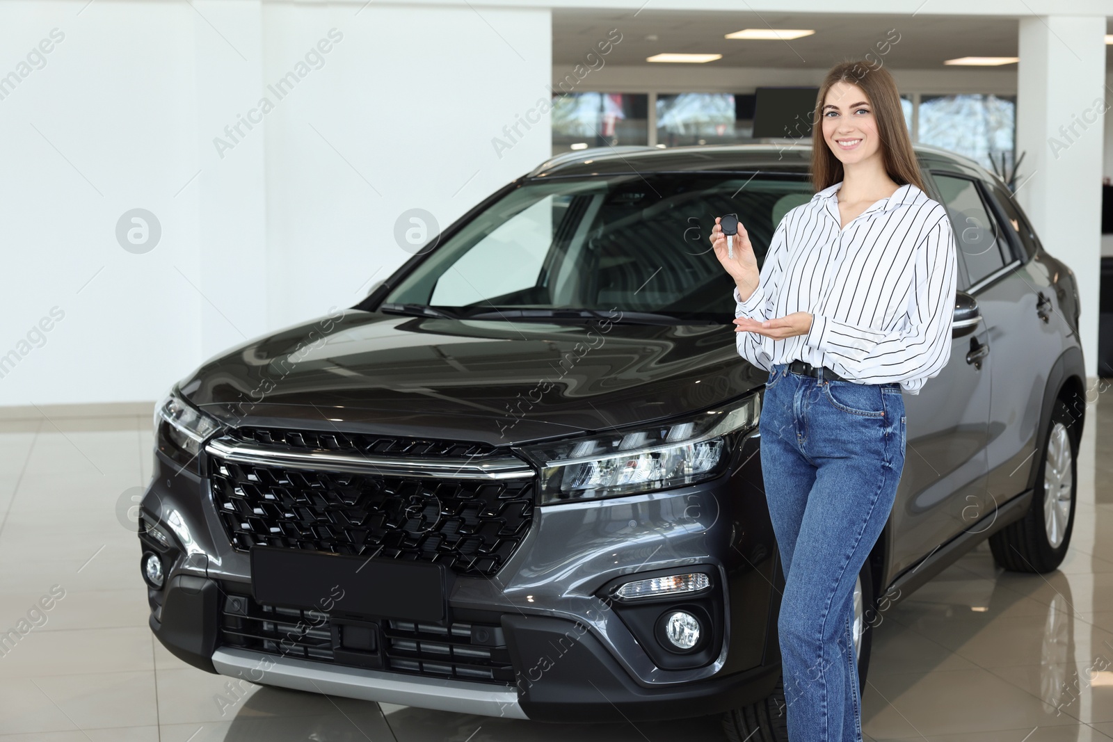 Photo of Happy young woman holding key near new black car in salon