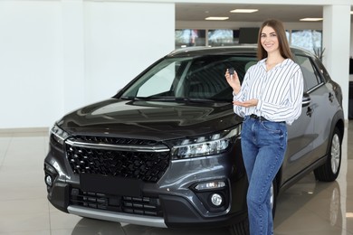 Photo of Happy young woman holding key near new black car in salon