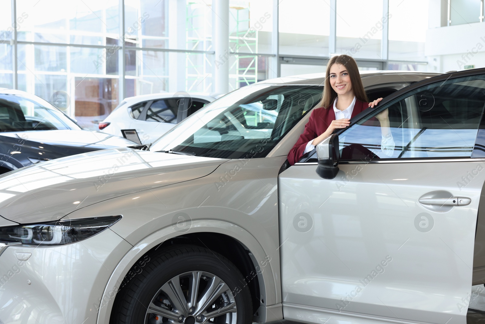 Photo of Happy saleswoman near new silver car in salon