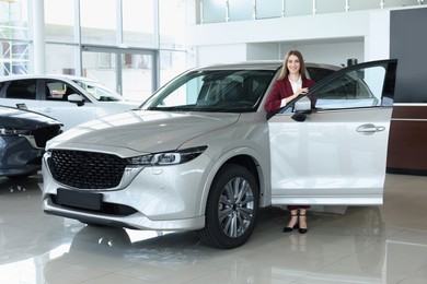 Happy saleswoman near new silver car in salon