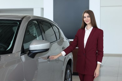 Photo of Happy saleswoman near new silver car in salon