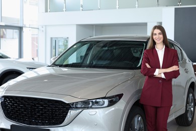 Photo of Happy saleswoman near new silver car in salon