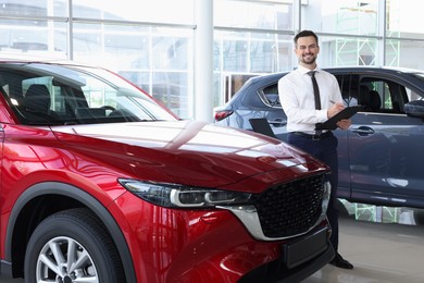 Photo of Happy salesman near new red car in salon